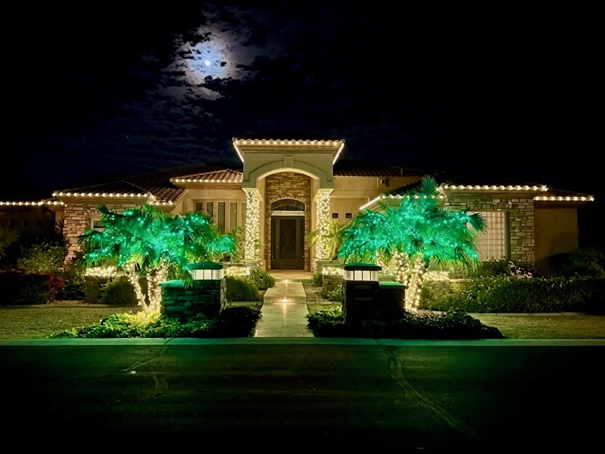 Christmas lights with green-lit palm trees and warm white roofline on a Phoenix home at night