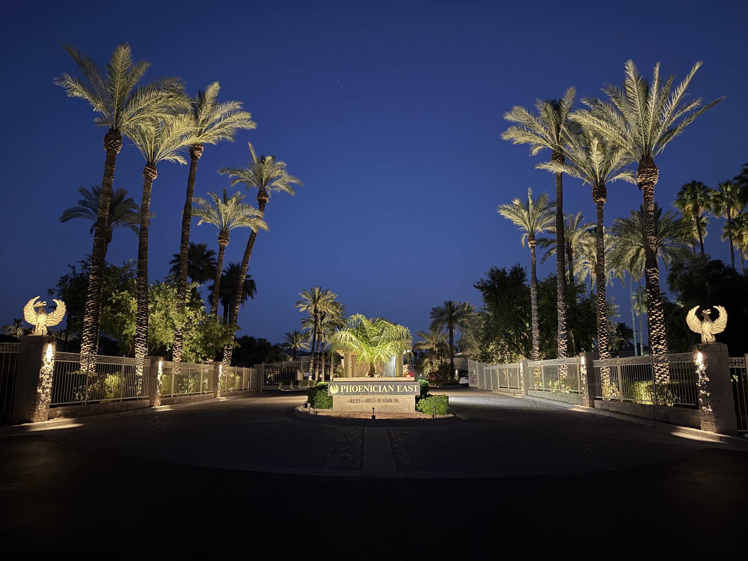 Upscale gated community entrance with palm uplighting and illuminated gates at night in Phoenix