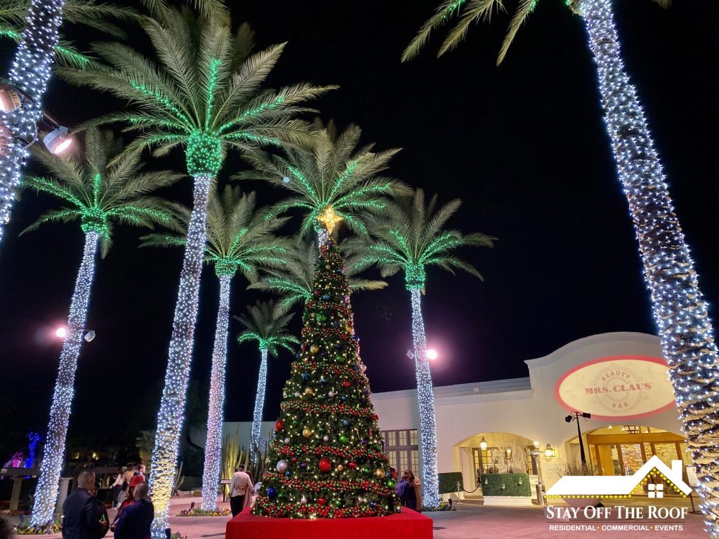 Commercial Christmas light installation by Stay Off The Roof at a Scottsdale, AZ shopping center — palm trees wrapped in white and green mini lights around a decorated Christmas tree