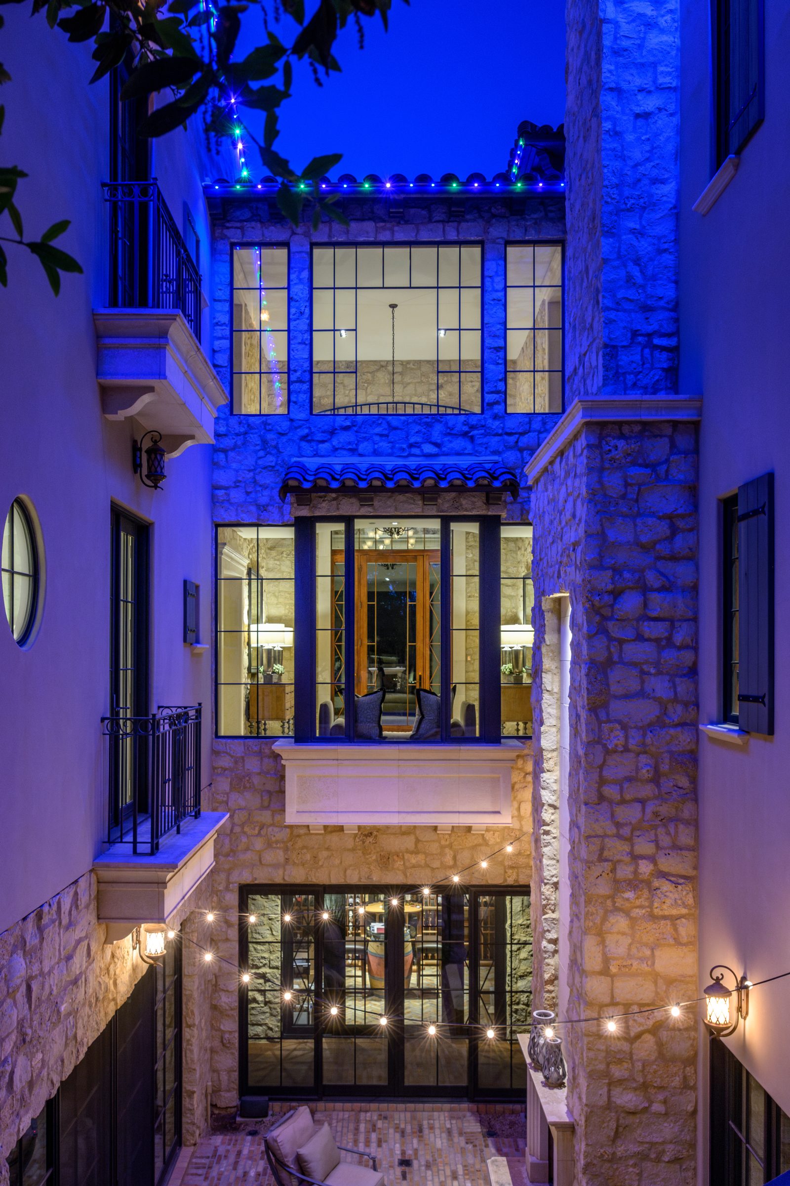 Blue permanent roofline lighting on a two-story stone and stucco estate at night