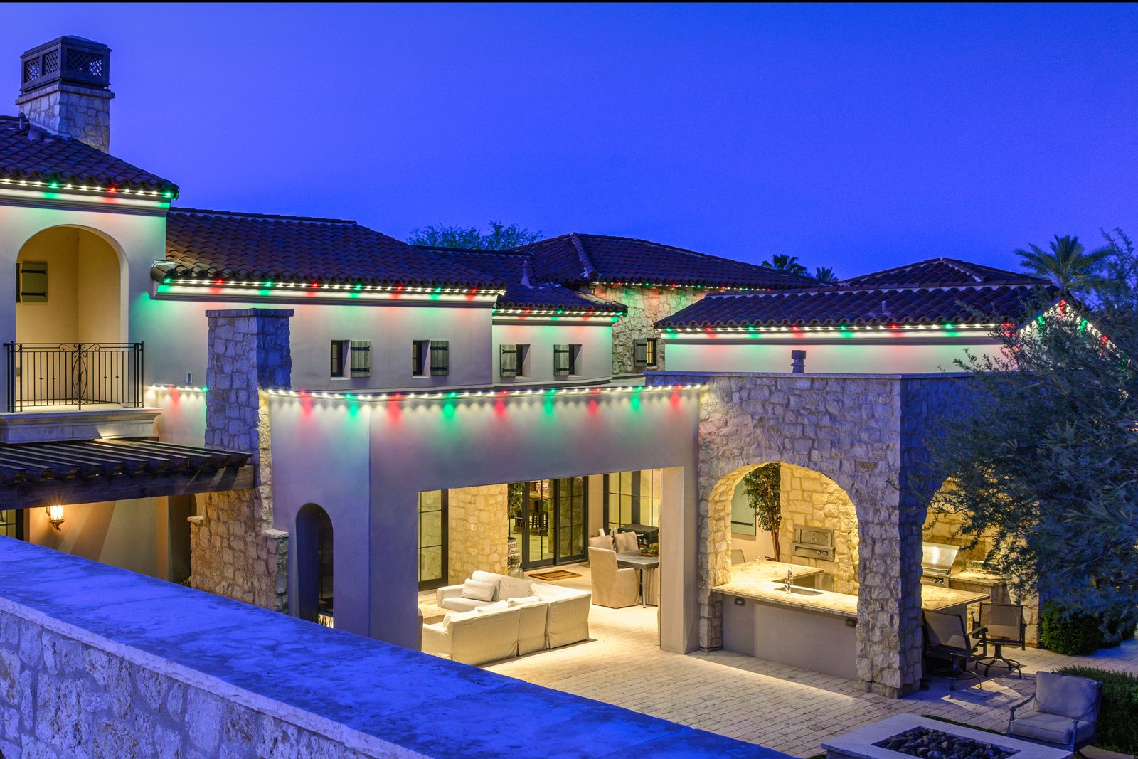 Red, green and white permanent Christmas lights along a long tile-roof roofline and covered patio