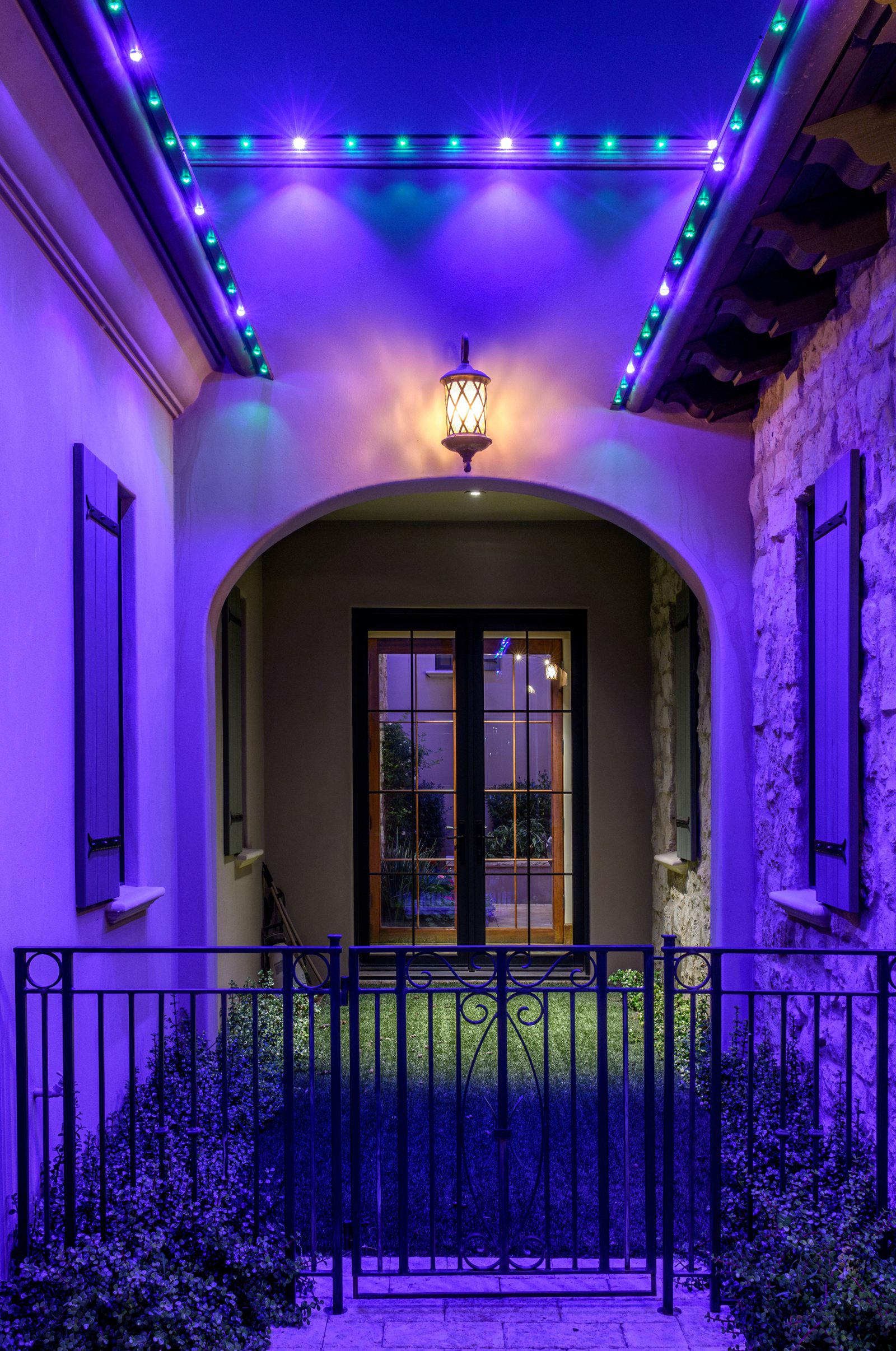 Purple permanent roofline lighting above an arched entry with wrought iron gate