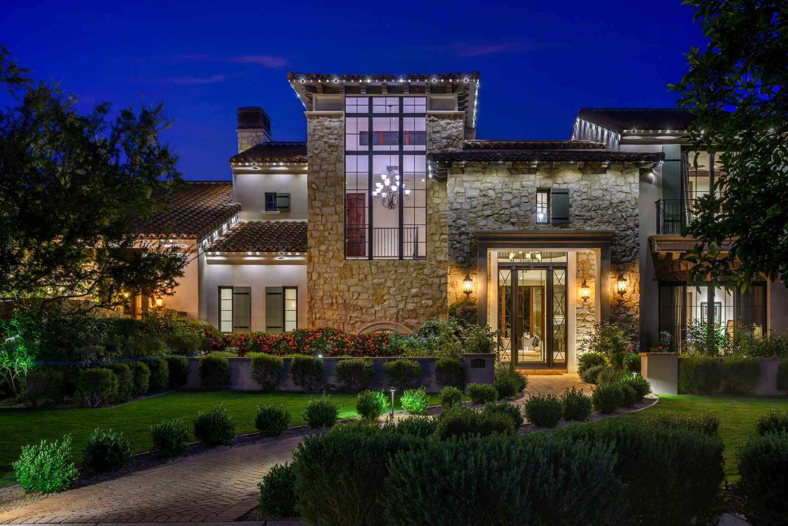Warm white permanent roofline lighting on a two-story stone estate at night