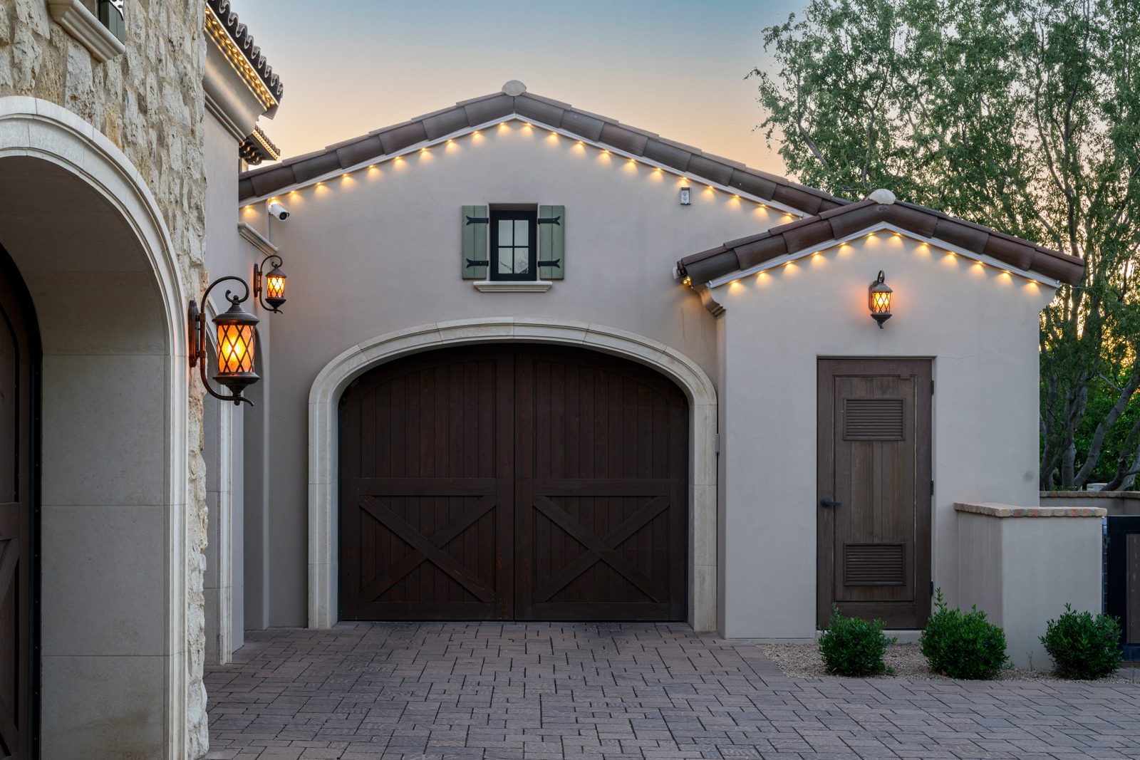 Warm white permanent trim lighting along a tile-roof garage at dusk