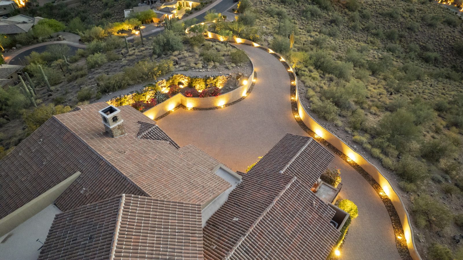 Aerial view of a lit pathway winding across a hillside desert property at night