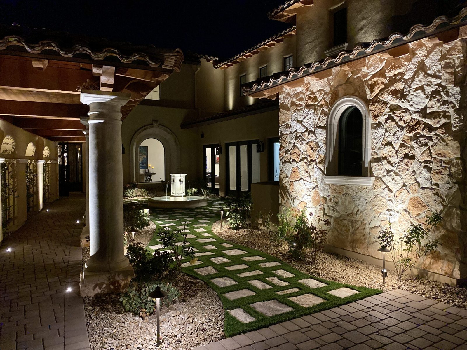 Mediterranean courtyard with lit columns, stepping stones and stone walls at night