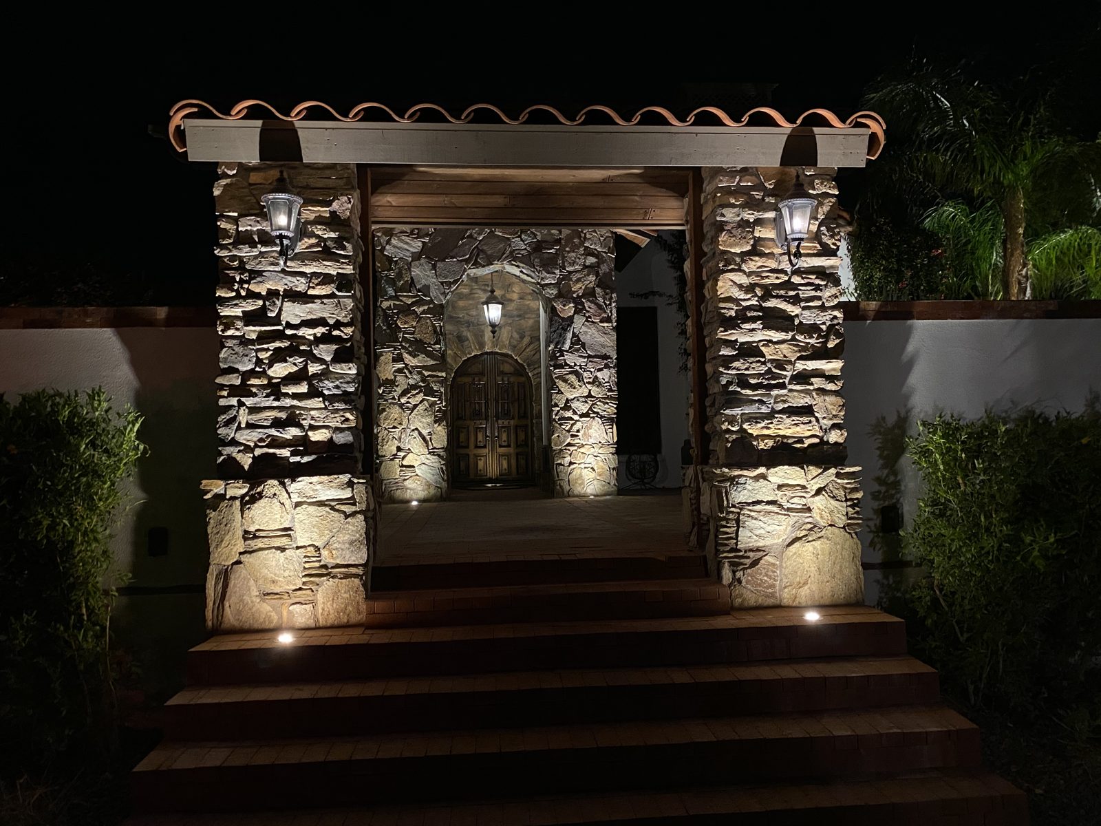 Stone entry pergola with uplit columns and step lights at night