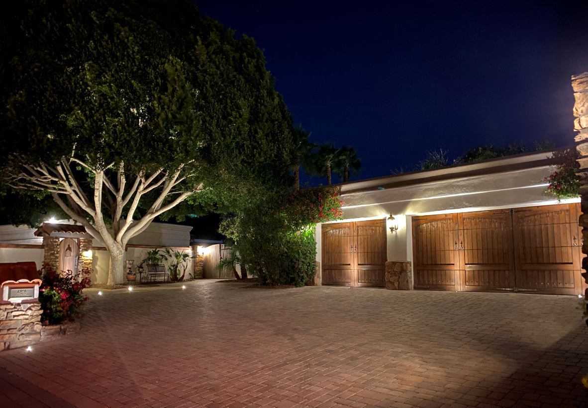 Uplit mature tree and wood garage doors on a paver driveway at night