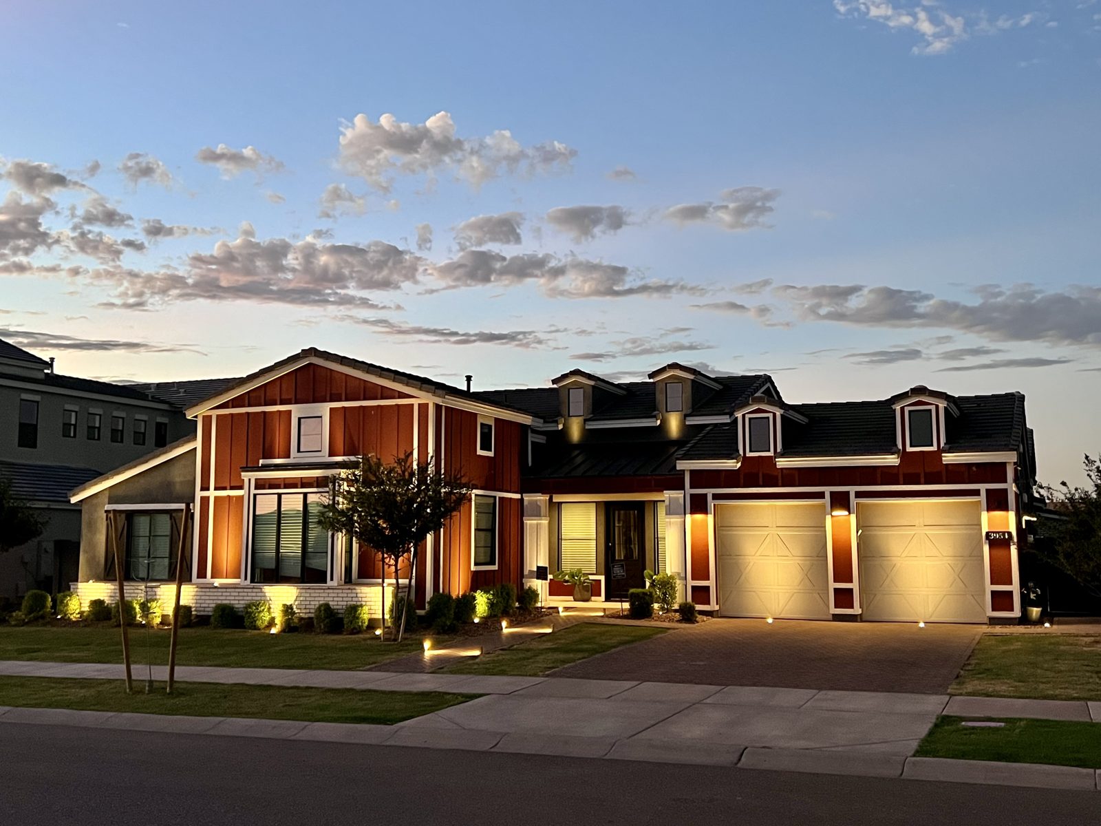 Two-story farmhouse-style home with warm facade and roofline lighting at dusk